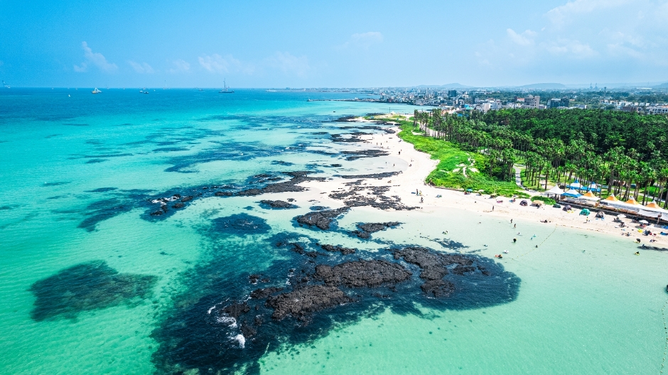 Hyeopjae Beach aerial view — turquoise water, white sand, black volcanic rocks